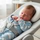 Newborn baby resting comfortably in inclined safety lounger with secure harness after feeding to help reduce reflux symptoms