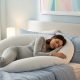 Pregnant woman sleeping comfortably on her side with white U-shaped pregnancy support pillow in peaceful bedroom setting