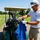 Golfer clipping a large microfiber golf towel onto a bag strap on a hot, sunny golf course during a summer round